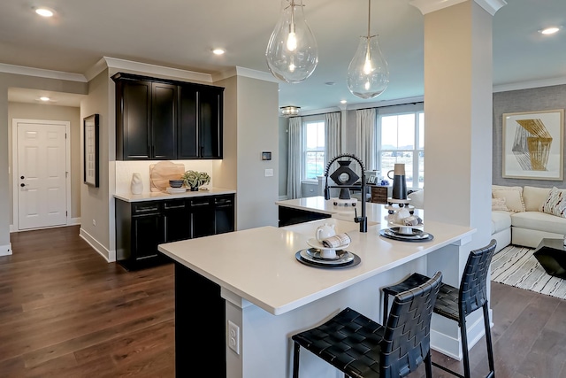 kitchen with a kitchen breakfast bar, crown molding, dark hardwood / wood-style flooring, and a center island with sink