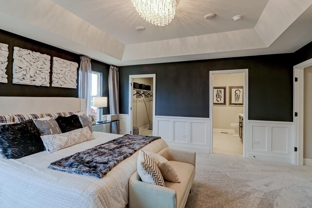 carpeted bedroom featuring ensuite bathroom, a raised ceiling, a spacious closet, and a notable chandelier