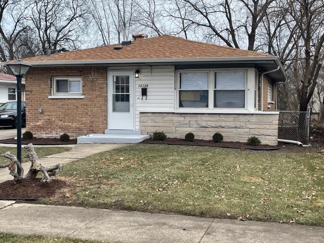 bungalow-style house featuring a shingled roof, a front yard, stone siding, and brick siding