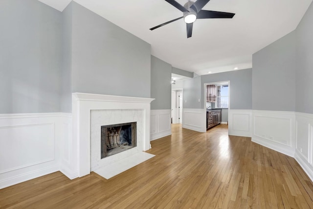 unfurnished living room with ceiling fan, light wood-type flooring, and a fireplace