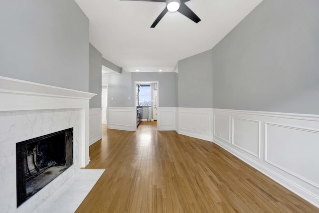 unfurnished living room with a premium fireplace, light wood-type flooring, and ceiling fan