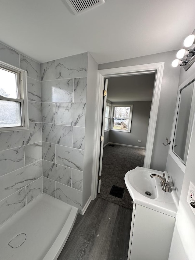 bathroom with hardwood / wood-style floors, vanity, a healthy amount of sunlight, and a tile shower