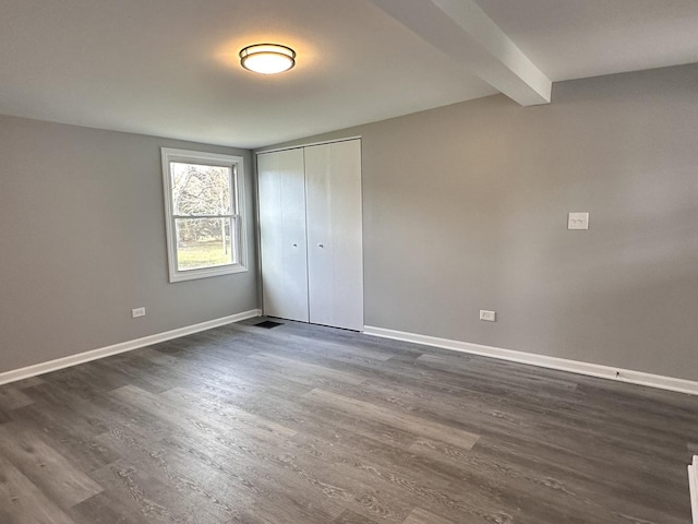 unfurnished bedroom with beamed ceiling, dark hardwood / wood-style floors, and a closet