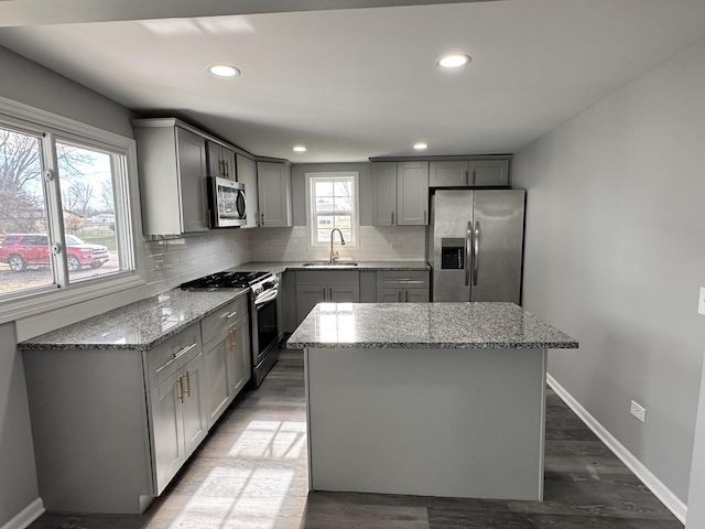 kitchen featuring gray cabinetry, light stone countertops, a center island, sink, and stainless steel appliances