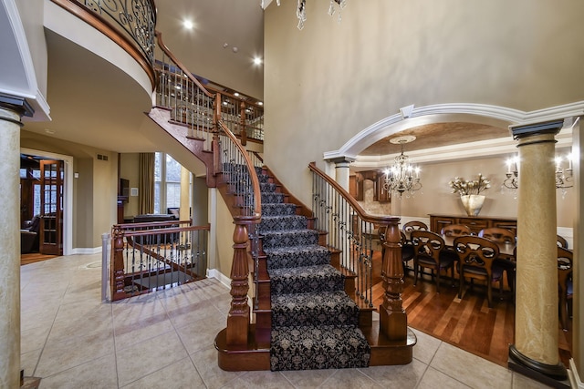 staircase with tile patterned floors, ornate columns, crown molding, and a high ceiling