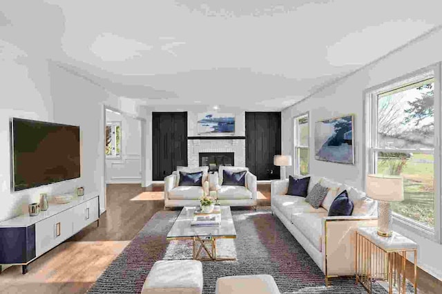 living room featuring plenty of natural light, wood-type flooring, and a brick fireplace