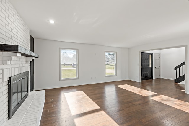 unfurnished living room featuring dark wood-type flooring and a brick fireplace