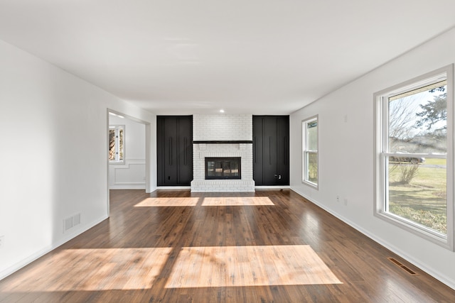 unfurnished living room with a brick fireplace and dark wood-type flooring