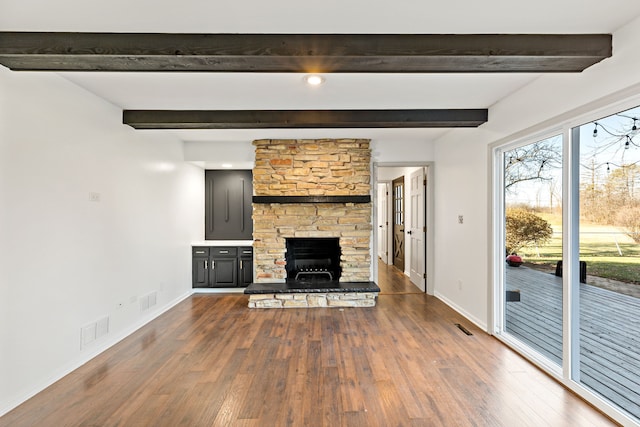 unfurnished living room featuring beam ceiling, a stone fireplace, and hardwood / wood-style floors