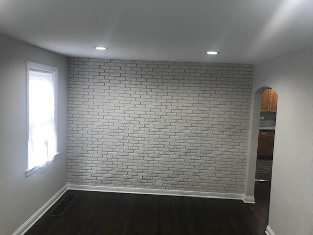 empty room featuring brick wall, dark wood-style flooring, visible vents, and baseboards