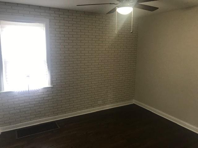 unfurnished room featuring brick wall, visible vents, baseboards, and dark wood finished floors