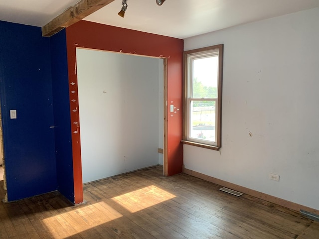 unfurnished bedroom featuring hardwood / wood-style floors and beam ceiling