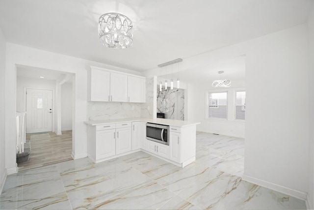 kitchen with backsplash, stainless steel microwave, white cabinets, decorative light fixtures, and kitchen peninsula