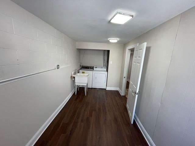 laundry area featuring washing machine and dryer, laundry area, dark wood-style flooring, a sink, and baseboards