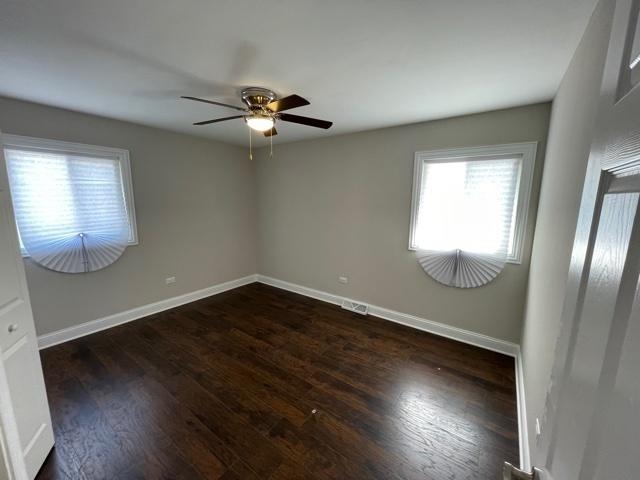 empty room featuring a ceiling fan, dark wood finished floors, and baseboards