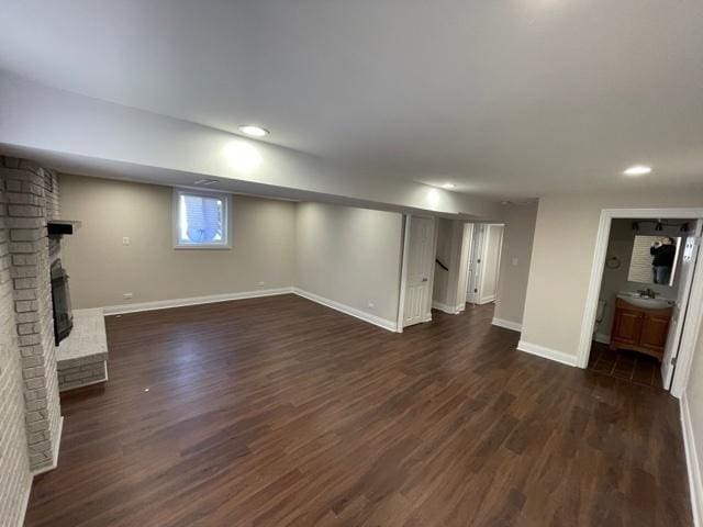 basement with dark wood-type flooring, recessed lighting, a brick fireplace, and baseboards