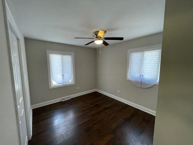 empty room featuring ceiling fan, visible vents, baseboards, and dark wood finished floors