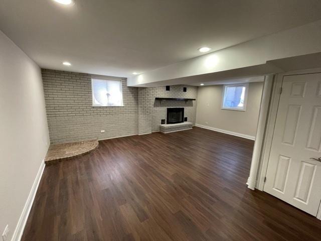 below grade area with dark wood-style floors, brick wall, plenty of natural light, and a fireplace