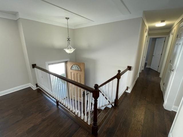 hallway with baseboards, ornamental molding, dark wood-type flooring, and an upstairs landing