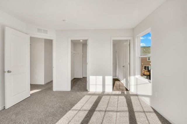 unfurnished bedroom featuring a walk in closet, light carpet, and a closet