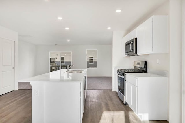 kitchen with light wood-type flooring, stainless steel appliances, sink, white cabinets, and an island with sink