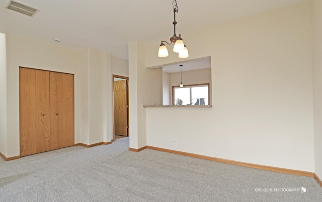 carpeted spare room featuring an inviting chandelier