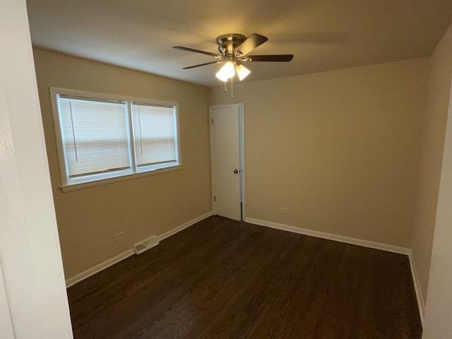 empty room featuring baseboards, visible vents, dark wood finished floors, and a ceiling fan