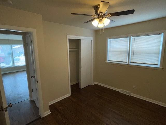 unfurnished bedroom featuring dark wood-style flooring, a ceiling fan, visible vents, baseboards, and a closet