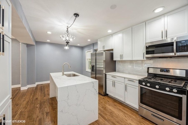 kitchen with white cabinets, sink, hardwood / wood-style flooring, an island with sink, and stainless steel appliances