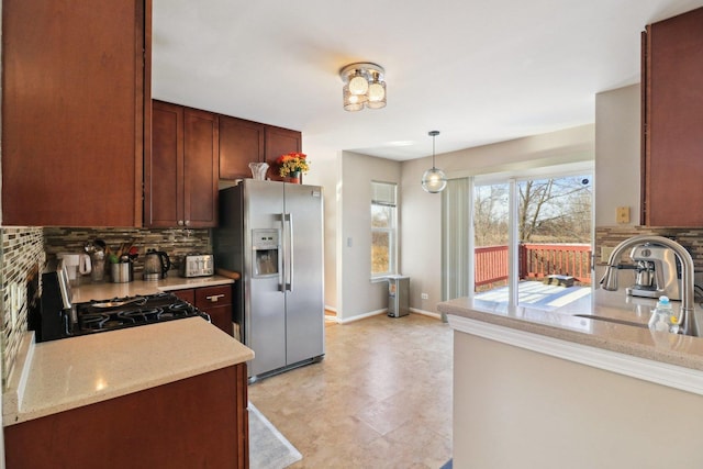 kitchen featuring range with gas cooktop, decorative light fixtures, backsplash, light stone counters, and stainless steel refrigerator with ice dispenser