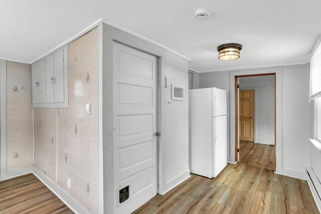 corridor with light wood-type flooring, baseboard heating, tile walls, and crown molding