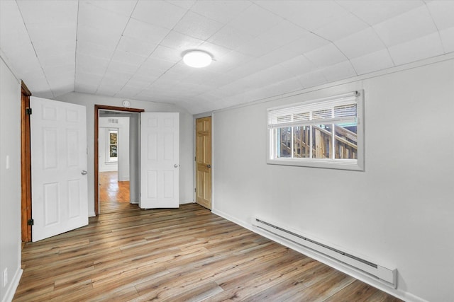 unfurnished room with vaulted ceiling, light hardwood / wood-style flooring, and a baseboard radiator