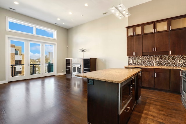 kitchen featuring appliances with stainless steel finishes, a center island, decorative backsplash, hanging light fixtures, and dark brown cabinets