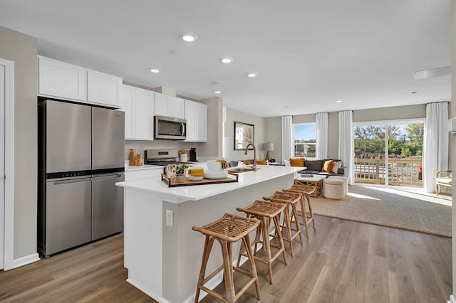 kitchen with a breakfast bar area, an island with sink, light hardwood / wood-style floors, white cabinetry, and stainless steel appliances