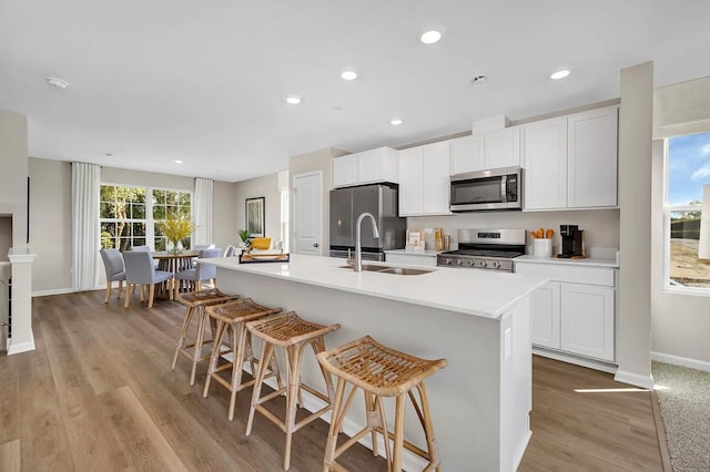 kitchen with white cabinets, appliances with stainless steel finishes, light hardwood / wood-style flooring, and a kitchen island with sink