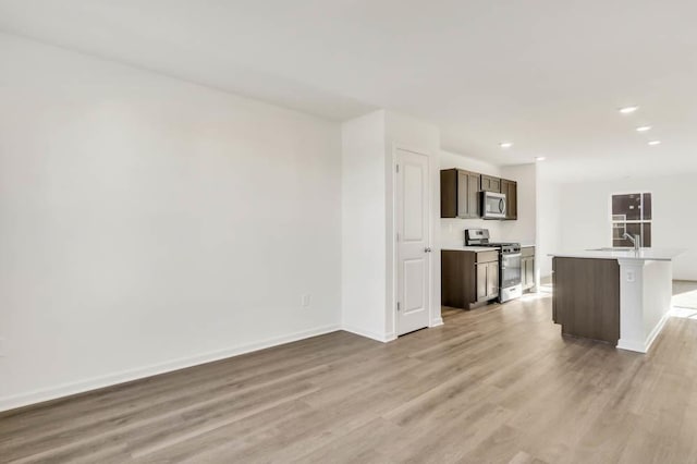 kitchen featuring dark brown cabinets, stainless steel appliances, sink, a center island with sink, and light hardwood / wood-style flooring