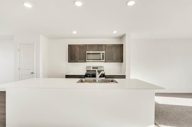 kitchen featuring sink, a kitchen island with sink, dark brown cabinets, carpet, and appliances with stainless steel finishes