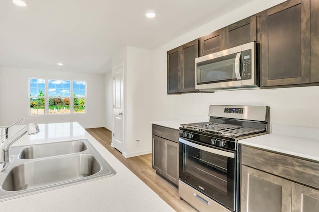 kitchen with dark brown cabinetry, sink, light wood-type flooring, and appliances with stainless steel finishes