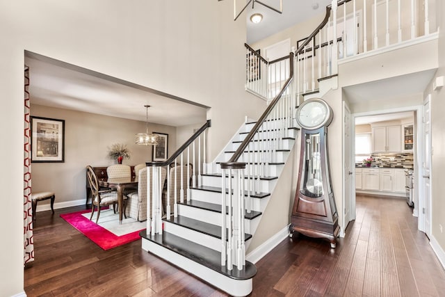 stairway with a towering ceiling, hardwood / wood-style floors, and a chandelier