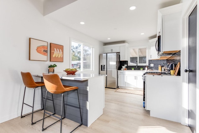 kitchen with a kitchen bar, white cabinets, light wood-type flooring, and appliances with stainless steel finishes