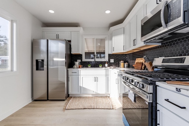 kitchen with backsplash, light wood-type flooring, stainless steel appliances, sink, and white cabinetry