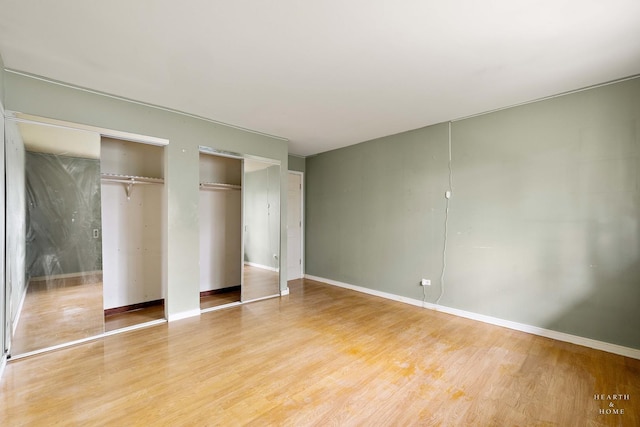 unfurnished bedroom with hardwood / wood-style flooring and multiple closets