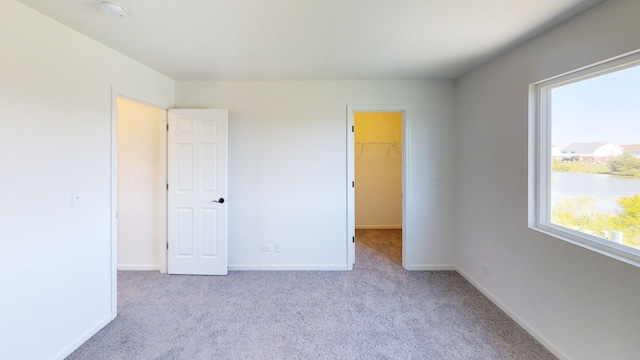 unfurnished bedroom featuring a walk in closet, light carpet, and a closet