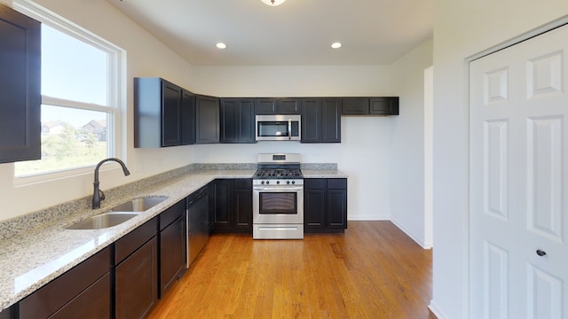 kitchen with light stone counters, sink, stainless steel appliances, and light hardwood / wood-style flooring