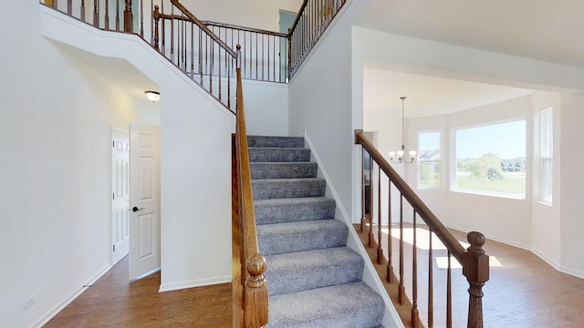 stairway with a notable chandelier, wood-type flooring, and a high ceiling