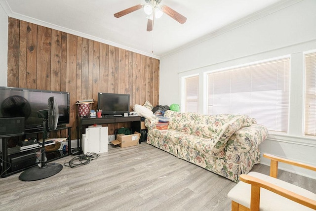 living room with crown molding, ceiling fan, wood walls, and light wood-type flooring