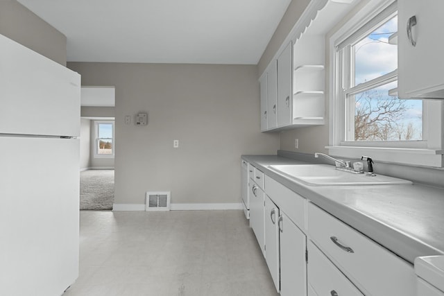 kitchen with white cabinets, light carpet, white fridge, and sink