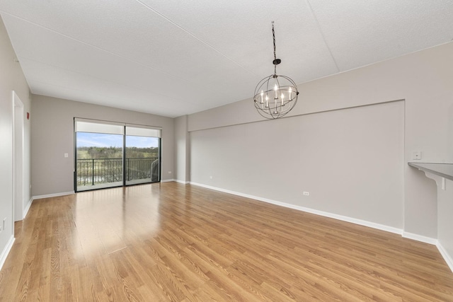 spare room featuring light wood-type flooring and a notable chandelier