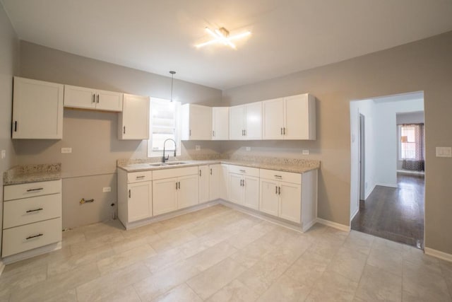 kitchen with sink, hanging light fixtures, light stone countertops, light wood-type flooring, and white cabinetry