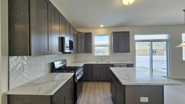 kitchen with light stone countertops, black gas stove, decorative backsplash, a kitchen island, and light wood-type flooring